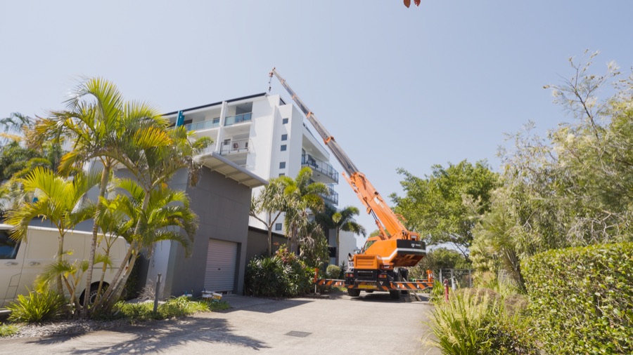 Crane lifting air conditioning equipment beside a multi storey apartment building