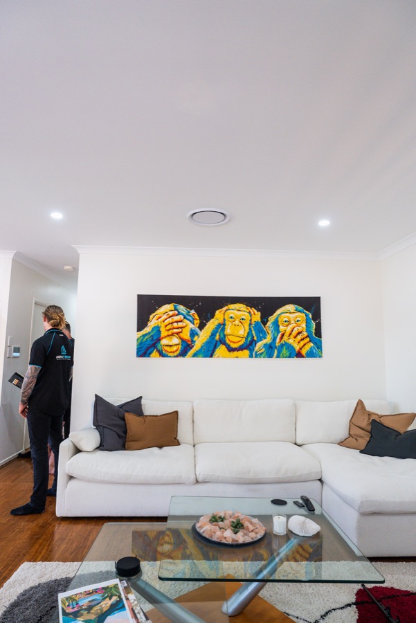 Living room with a round ducted air conditioning outlet in the ceiling and a technician at the wall controller
