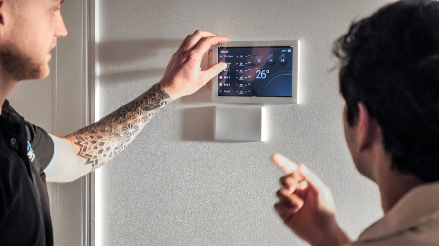 Technician showing a homeowner the zone controller on the wall, set to 26 degrees