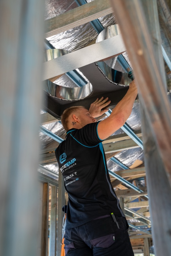Delta Temp technician fitting ducting to a ceiling plenum in a new home frame