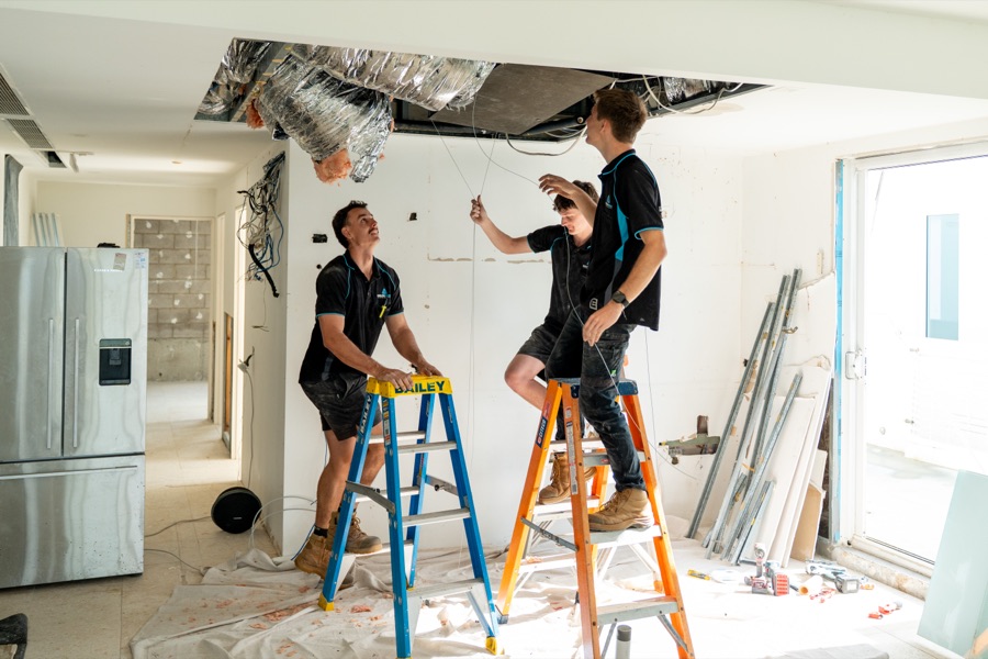 Two technicians on ladders fitting a ducted system through an open ceiling